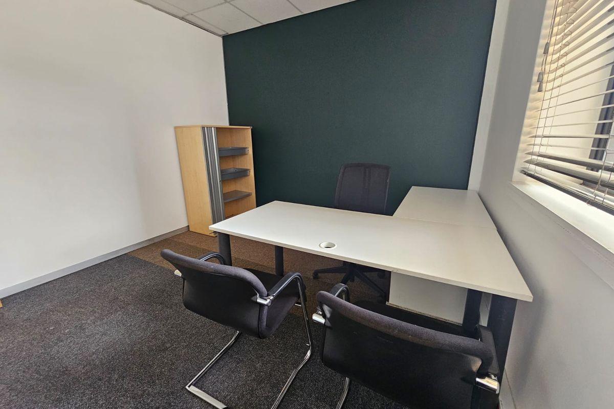 A functional office space featuring a suspended ceiling, carpeted flooring, and venetian blinds, providing a professional environment for business operations.