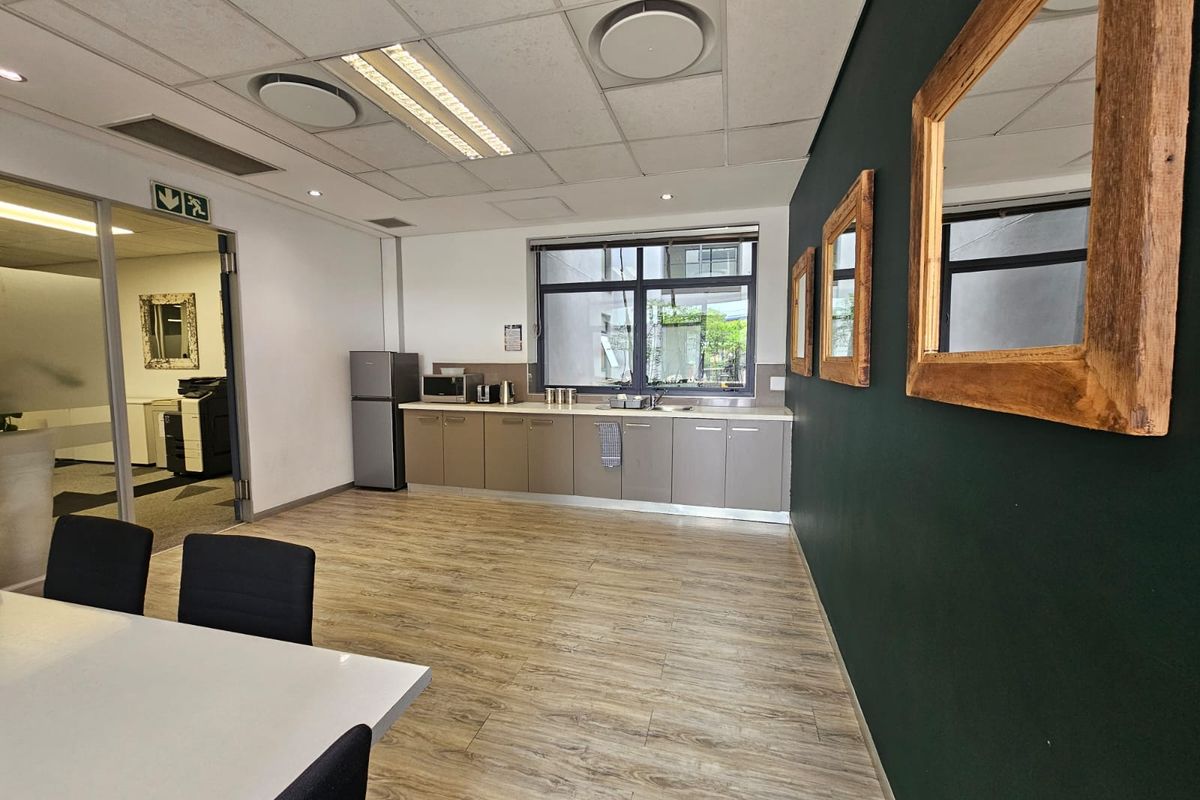 A functional office kitchenette featuring built-in cabinetry, laminate countertops, a stainless steel sink, and modern laminate flooring in a professional workspace.