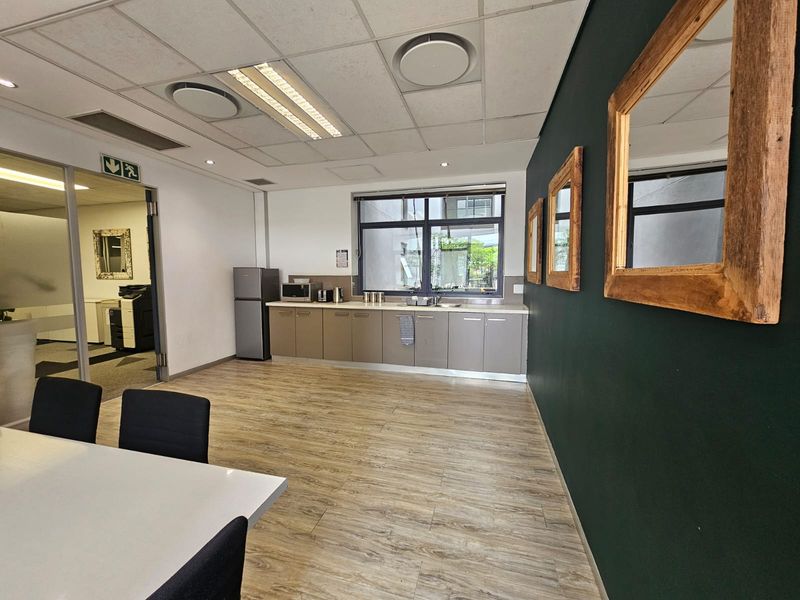 A functional office kitchenette featuring built-in cabinetry, laminate countertops, a stainless steel sink, and modern laminate flooring in a professional workspace.