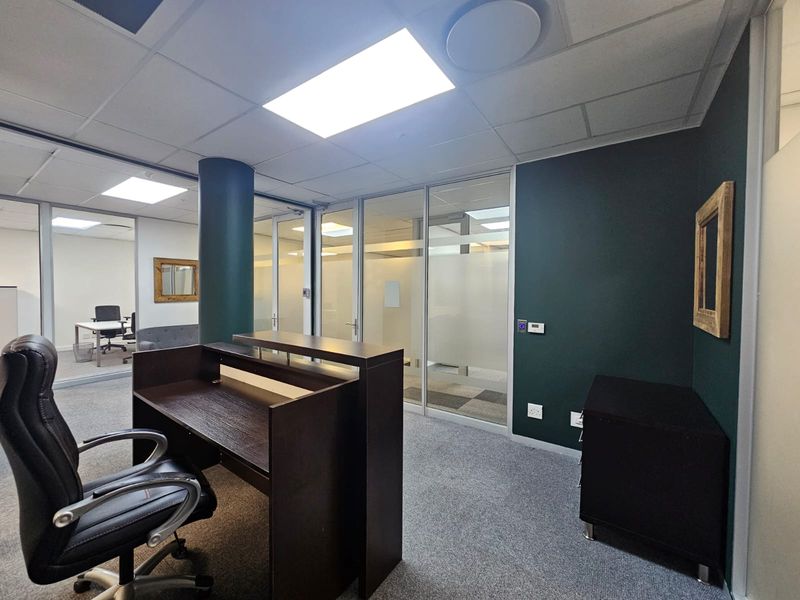 Modern office space featuring glass partitioning, suspended ceilings with recessed lighting, and carpeted flooring, providing a professional and well-lit work environment.