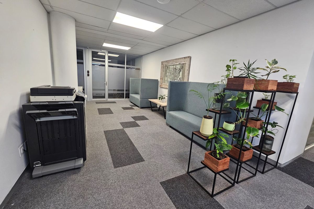 A functional office reception or waiting area featuring a suspended ceiling, recessed lighting, and modern carpet tiles with a glass partition entrance.