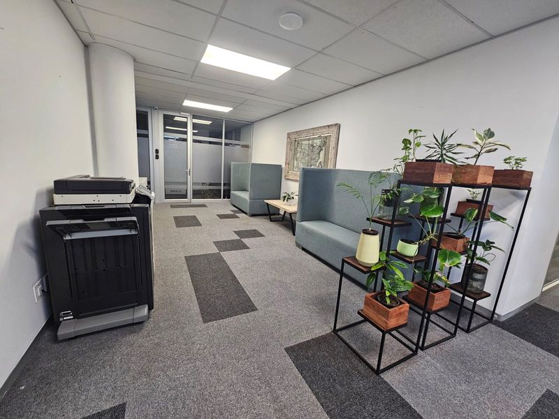 A functional office reception or waiting area featuring a suspended ceiling, recessed lighting, and modern carpet tiles with a glass partition entrance.