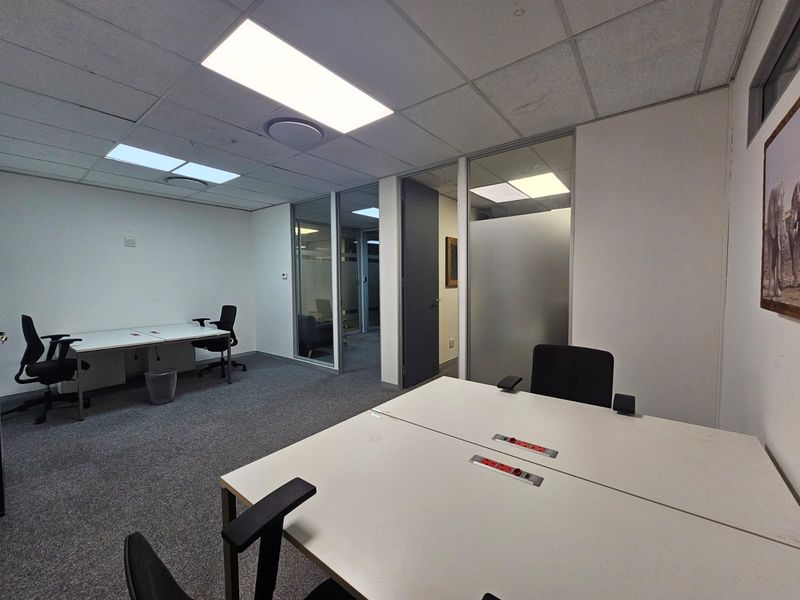 A professional office space featuring glass partitions, suspended ceilings with recessed lighting, and carpeted flooring, providing a clean and functional work environment.
