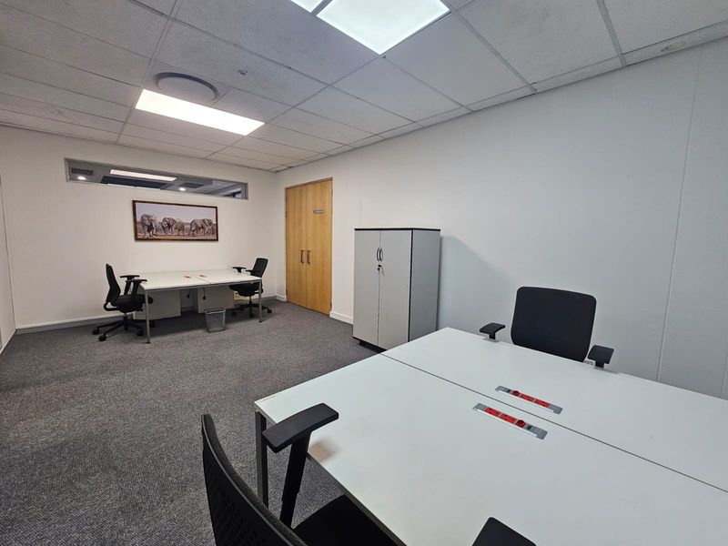 A functional office space featuring carpeted flooring, a suspended ceiling with recessed lighting, and double wooden doors.