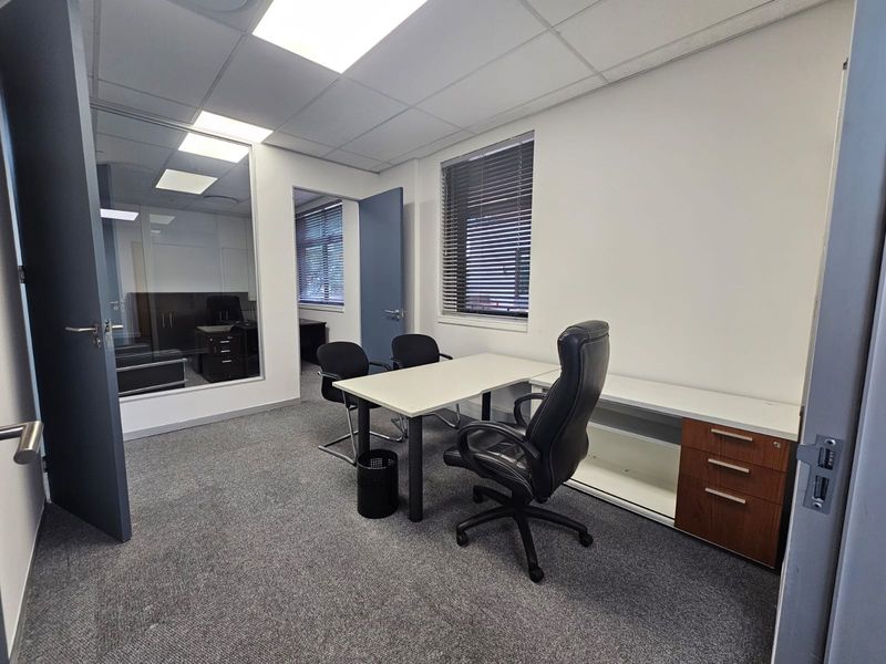 A professional office space featuring a built-in desk, glass partition wall, carpeted flooring, and recessed ceiling lighting, providing a functional workspace environment.