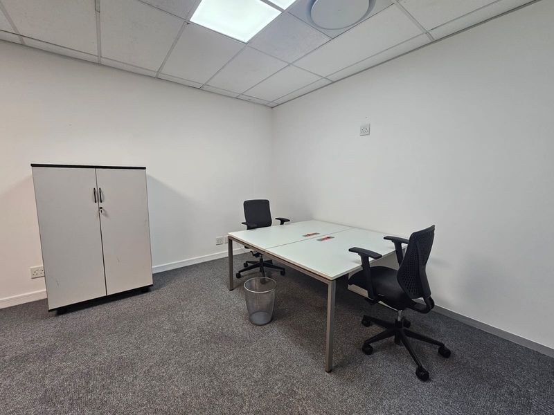 A functional office space featuring a suspended ceiling, recessed lighting, and neutral carpet flooring, suitable for a professional work environment.