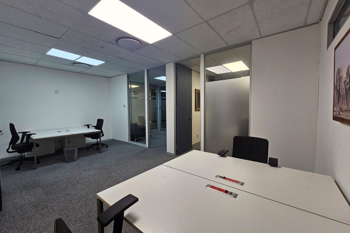 A professional office space featuring glass partitions, suspended ceilings with recessed lighting, and carpeted flooring, providing a clean and functional work environment.
