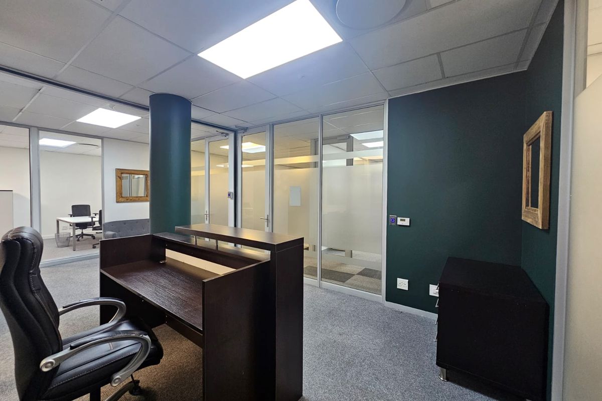 Modern office space featuring glass partitioning, suspended ceilings with recessed lighting, and carpeted flooring, providing a professional and well-lit work environment.