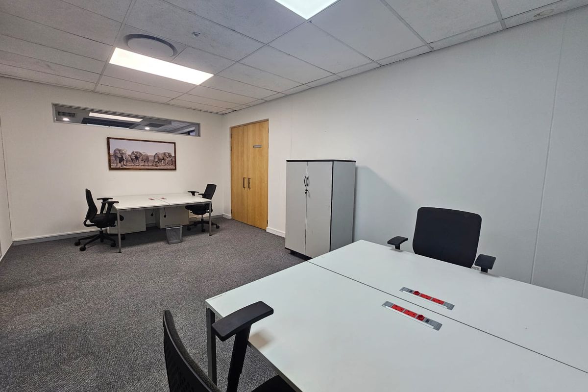 A functional office space featuring carpeted flooring, a suspended ceiling with recessed lighting, and double wooden doors.