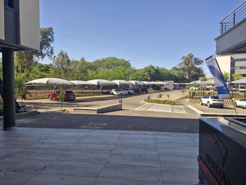 Commercial parking area featuring multiple shade cloth carports, paved driveway, and a tiled patio area in the foreground.