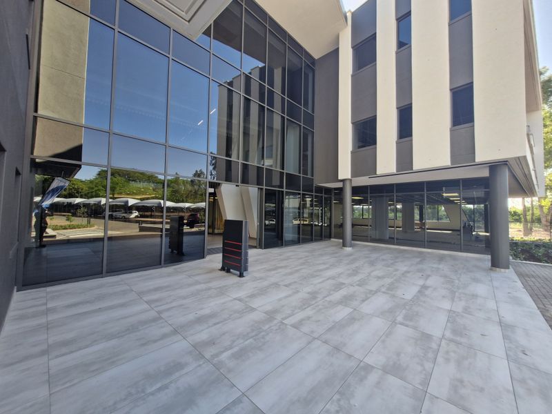Modern commercial building entrance featuring a large glass curtain wall facade and a spacious tiled patio area.