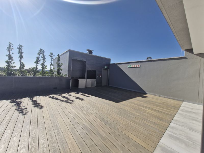 Spacious outdoor terrace featuring modern timber decking, a built-in braai area, and clear emergency exit signage, ideal for commercial entertainment or break-out space.