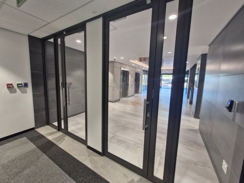 Modern commercial building entrance lobby featuring glass-panelled doors, tiled flooring, and professional elevator access area with contemporary finishes.
