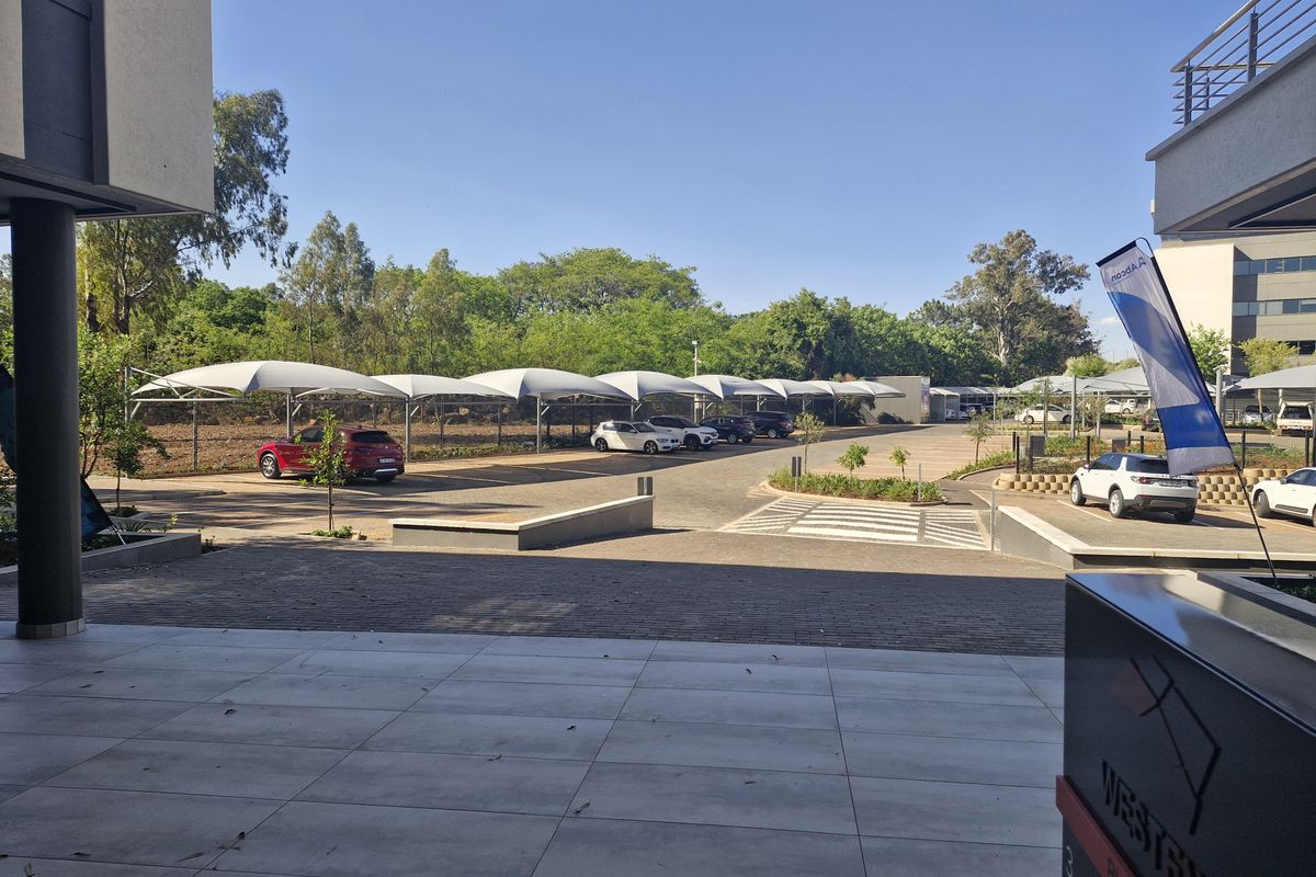 Commercial parking area featuring multiple shade cloth carports, paved driveway, and a tiled patio area in the foreground.