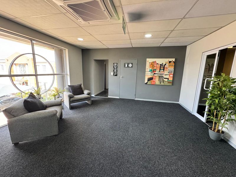 A professional office waiting area featuring carpeted flooring, a suspended ceiling with integrated air conditioning, and large windows providing natural light.
