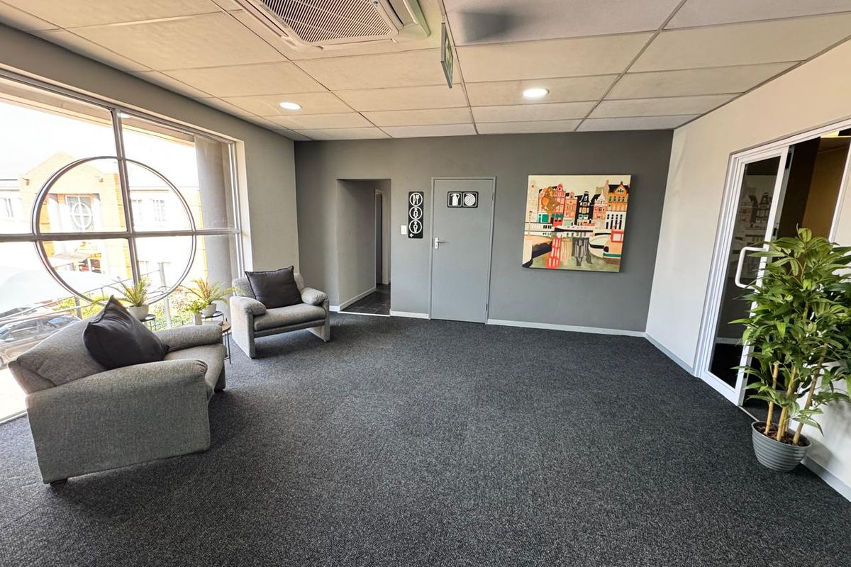 A professional office waiting area featuring carpeted flooring, a suspended ceiling with integrated air conditioning, and large windows providing natural light.