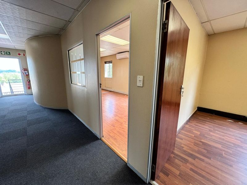 Empty office space featuring laminate and carpeted flooring, suspended ceilings, and a wall-mounted air conditioning unit, providing a functional workspace environment.