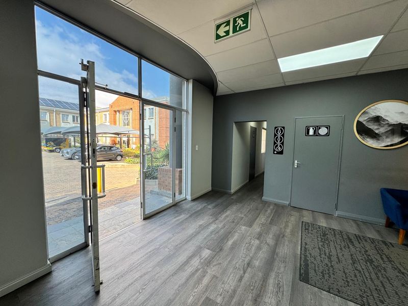 A bright and modern office entrance area featuring large glass doors, durable laminate flooring, and clear directional signage.