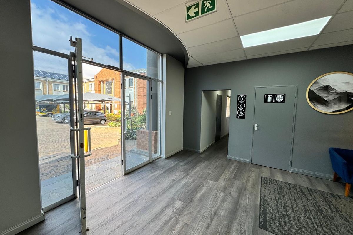 A bright and modern office entrance area featuring large glass doors, durable laminate flooring, and clear directional signage.