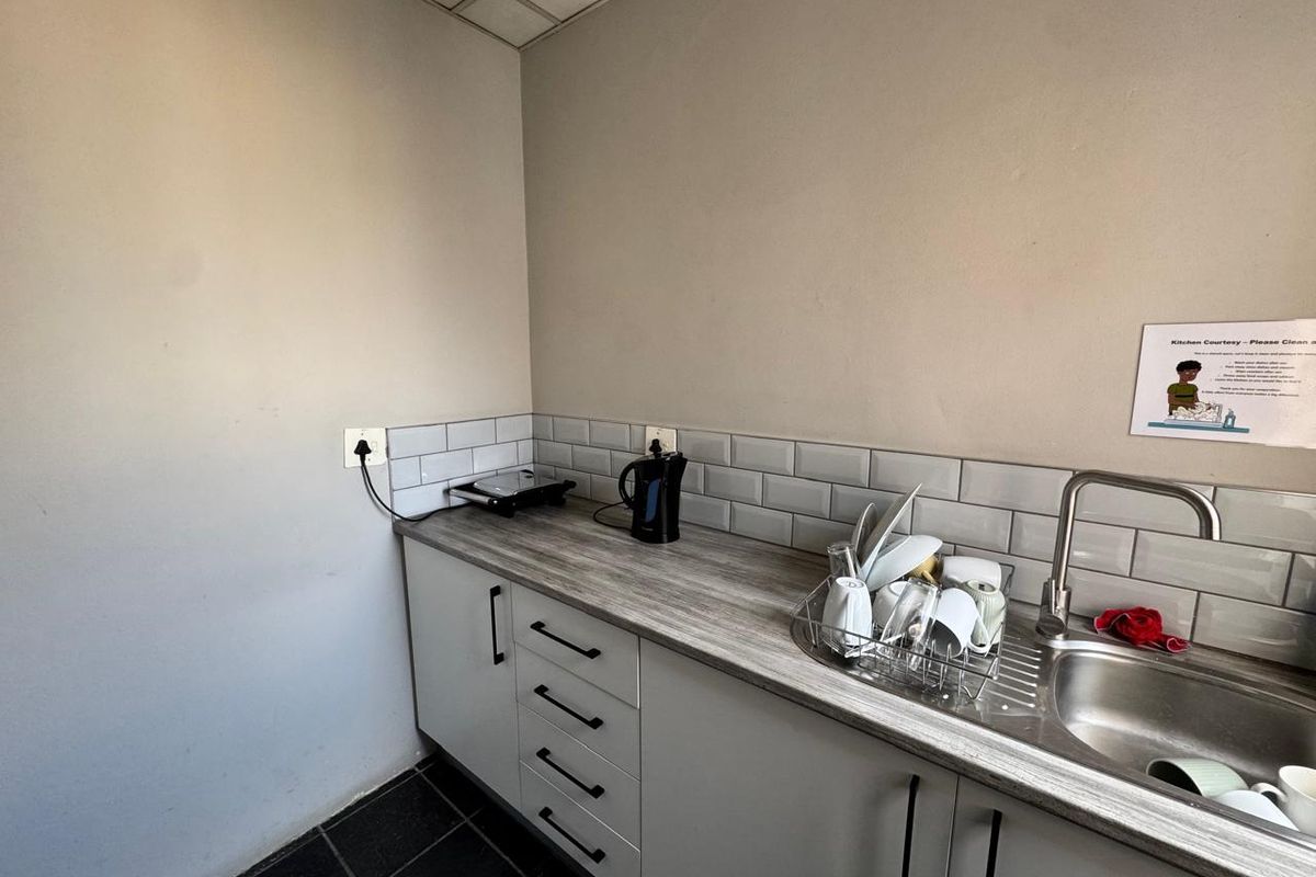 A compact office kitchenette featuring grey subway tile backsplash, laminate countertops, stainless steel sink, and modern cabinetry.