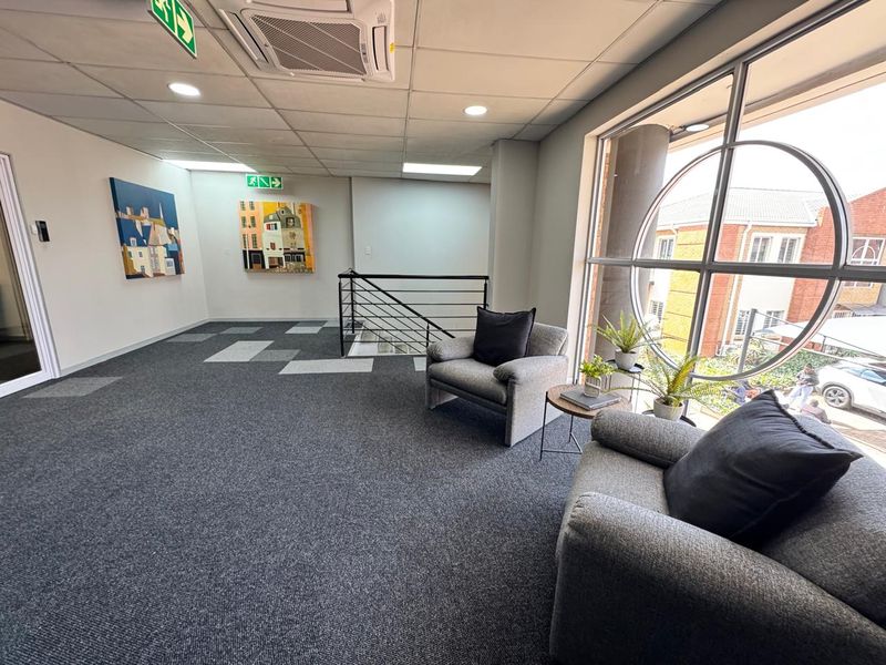 A bright office landing area featuring a large circular window, suspended ceiling with integrated air conditioning, and modern carpeted flooring.