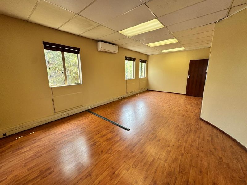 A vacant office space featuring laminate wood flooring, a suspended ceiling with recessed lighting, and a wall-mounted air conditioning unit.