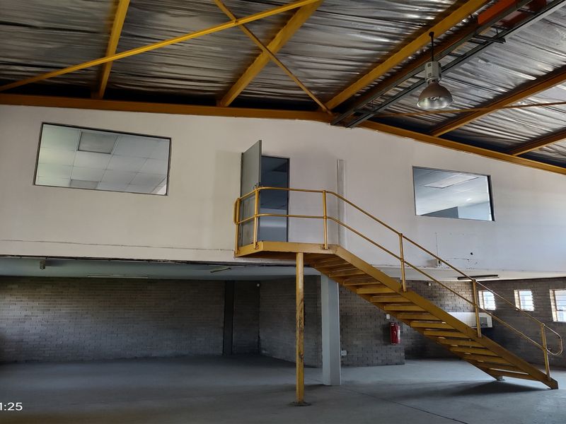 Spacious industrial warehouse unit featuring a mezzanine level with steel staircase, exposed roof trusses, and functional brick wall construction.
