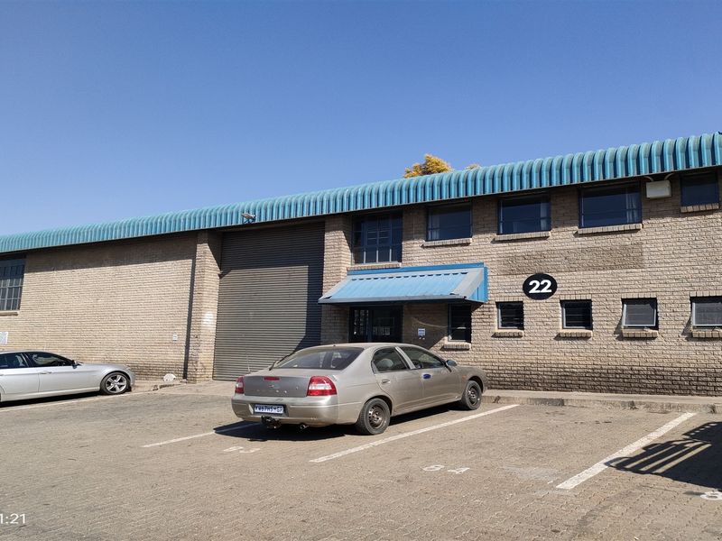 Front elevation of an industrial warehouse unit featuring a roller shutter door, brick facade, and dedicated paved parking bays.