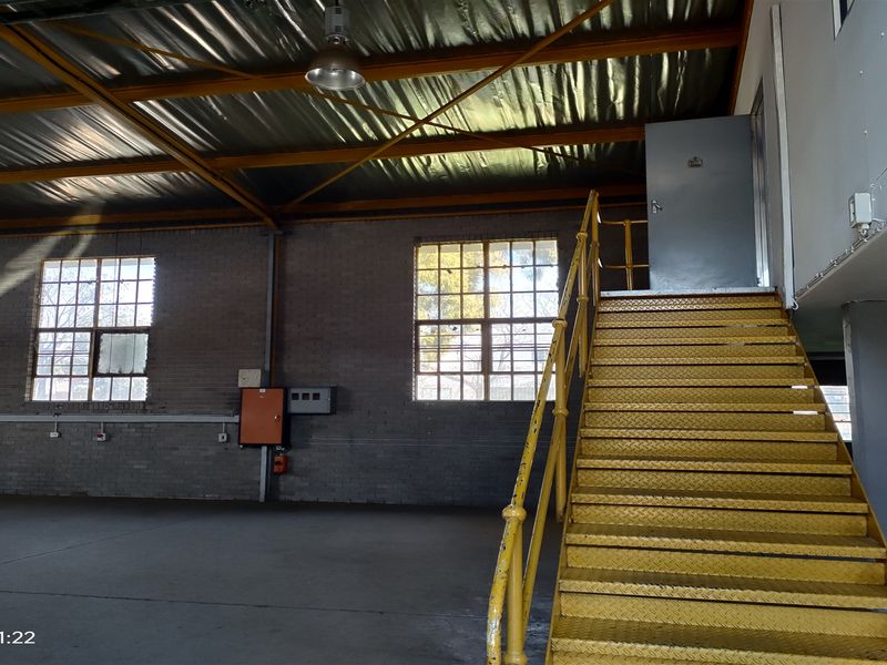 Spacious industrial utility area featuring exposed steel roof trusses, concrete flooring, and a prominent yellow metal staircase leading to an upper level.