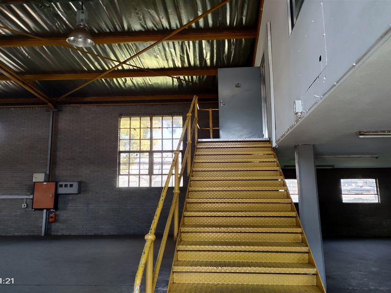 Spacious industrial utility area featuring exposed steel roof trusses, brick walls, and a prominent yellow metal staircase leading to an upper level.