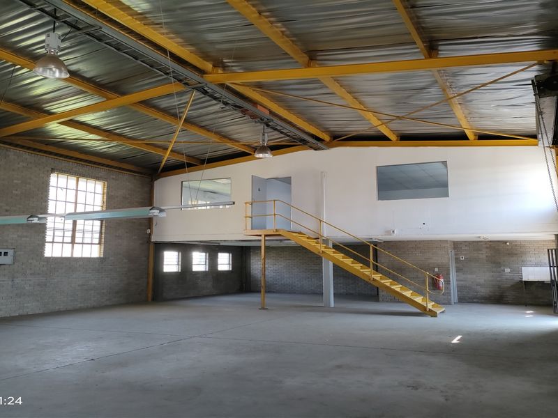 Spacious industrial warehouse unit featuring high ceilings with exposed steel trusses, a mezzanine level with staircase, and durable concrete flooring.