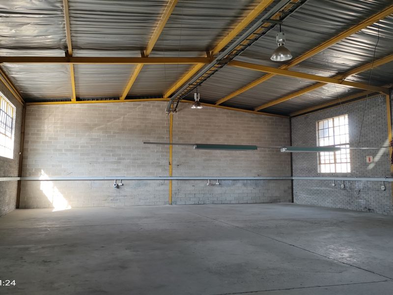 Spacious industrial warehouse unit featuring high ceilings with exposed steel trusses, concrete block walls, concrete flooring, and functional industrial lighting.