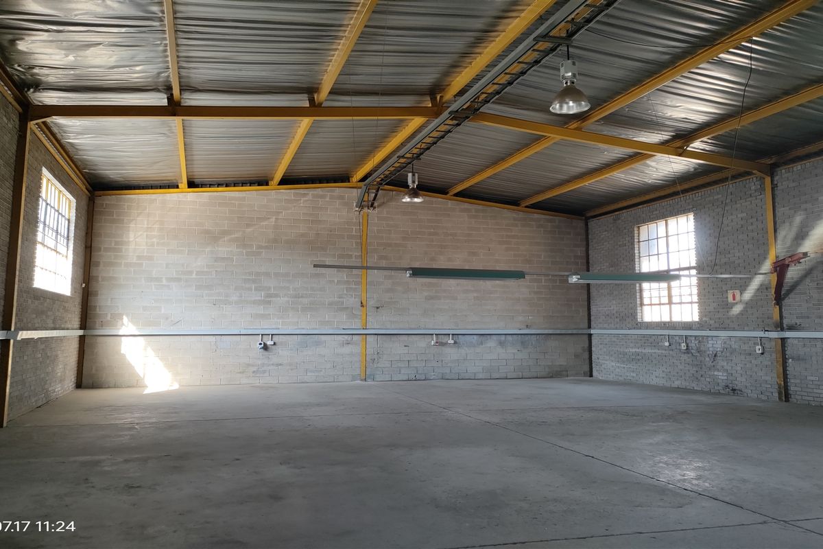 Spacious industrial warehouse unit featuring high ceilings with exposed steel trusses, concrete block walls, concrete flooring, and functional industrial lighting.