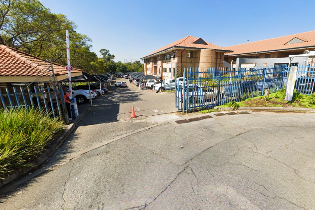 Exterior view of the office property entrance featuring a paved driveway, security fencing, access control gate, and covered parking areas.
