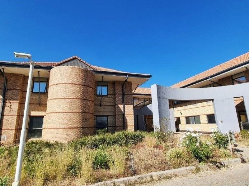 Front exterior view of a commercial office building featuring face brick construction, a tiled roof, and a paved driveway with established landscaping.