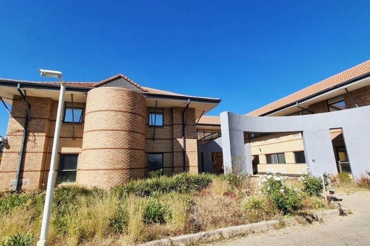 Front exterior view of a commercial office building featuring face brick construction, a tiled roof, and a paved driveway with established landscaping.