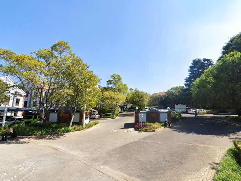 Street view of the office property entrance featuring a paved driveway, landscaped gardens, and covered parking facilities.