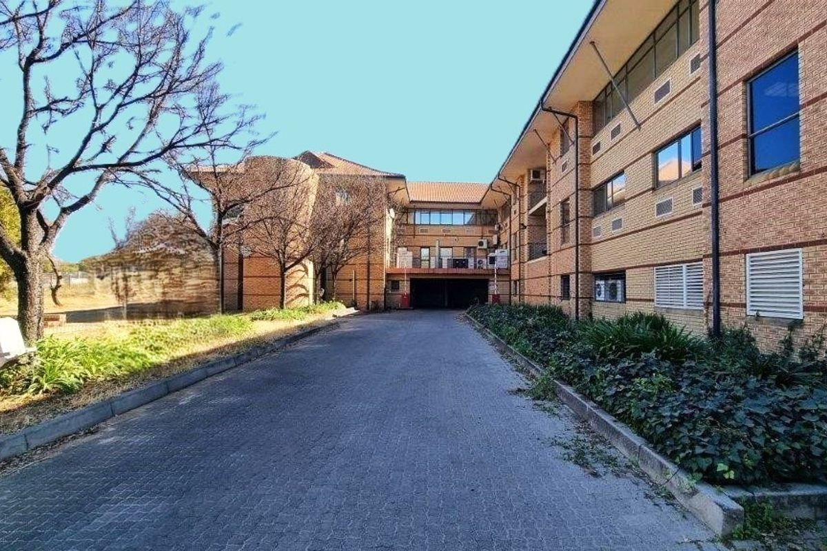 Rear view of a multi-story brick office building featuring a paved driveway, covered parking access, and established garden beds.