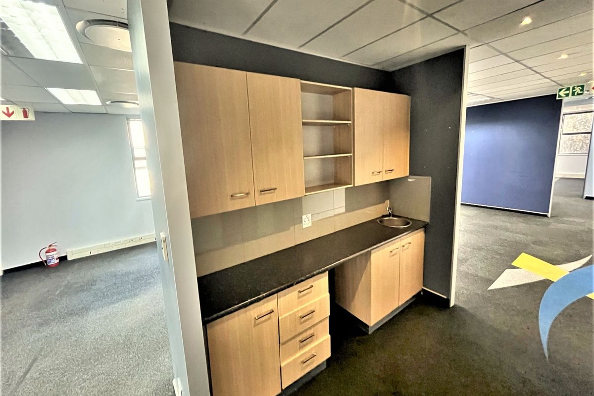 A functional office kitchenette featuring light wood cabinetry, a dark laminate countertop, and a small stainless steel sink.