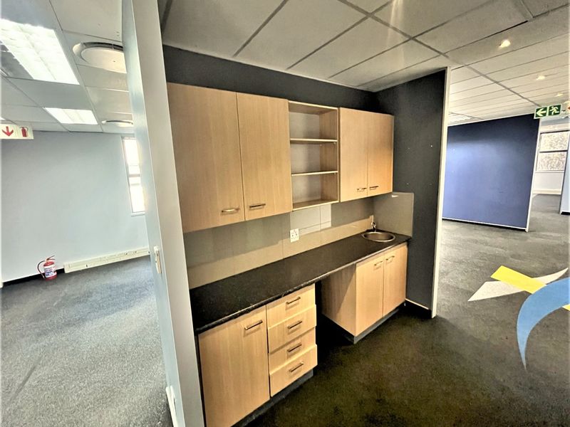 A functional office kitchenette featuring light wood cabinetry, a dark laminate countertop, and a small stainless steel sink.