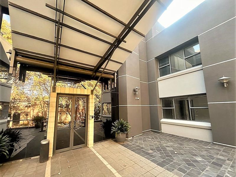 Modern office building entrance featuring a prominent metal canopy, glass double doors, and a paved courtyard area with exterior lighting.