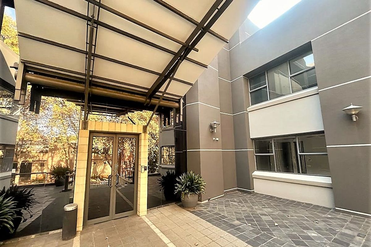 Modern office building entrance featuring a prominent metal canopy, glass double doors, and a paved courtyard area with exterior lighting.