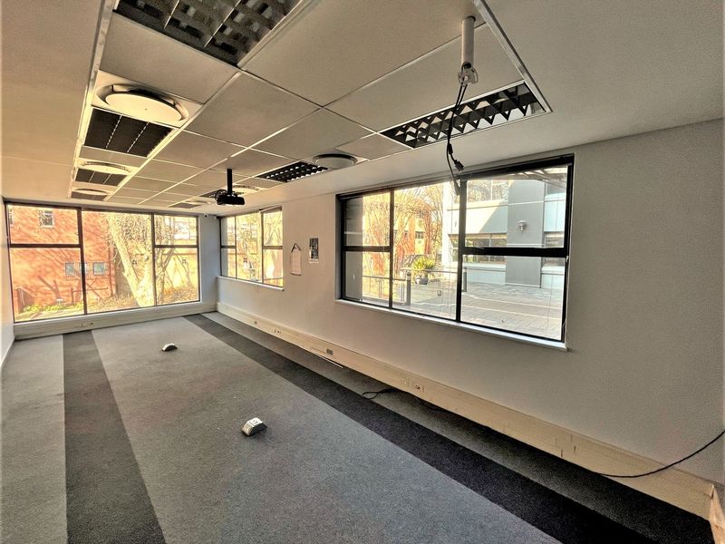 A vacant office space featuring large windows, carpeted flooring, and a suspended ceiling with integrated lighting and perimeter trunking.
