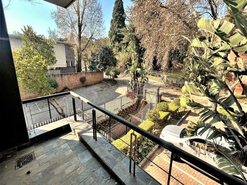 A balcony with stone tile flooring and a metal balustrade, overlooking the office property's parking area and landscaped grounds.