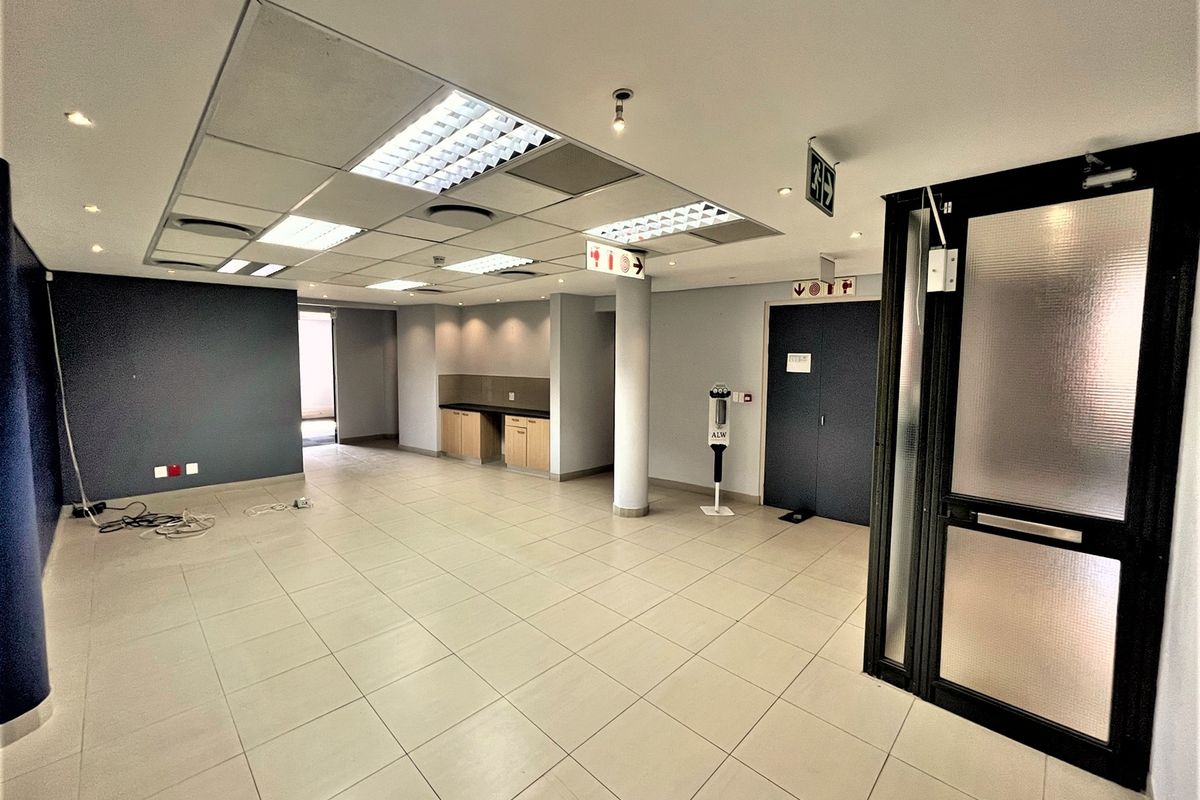 Spacious open-plan office area featuring tiled flooring, a suspended ceiling with recessed lighting, and a small built-in kitchenette unit.