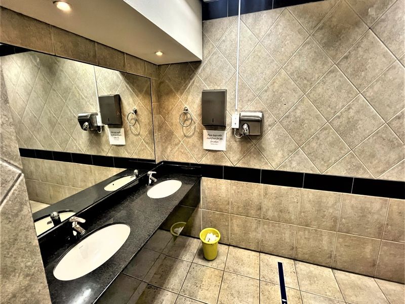 A clean, functional office bathroom featuring a dual vanity with granite countertops, large wall mirror, and tiled finishes throughout.