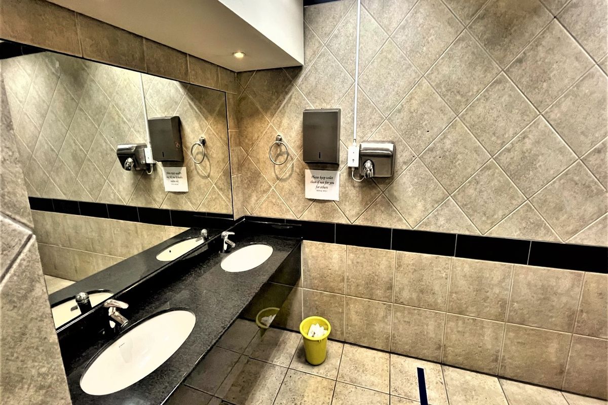 A clean, functional office bathroom featuring a dual vanity with granite countertops, large wall mirror, and tiled finishes throughout.