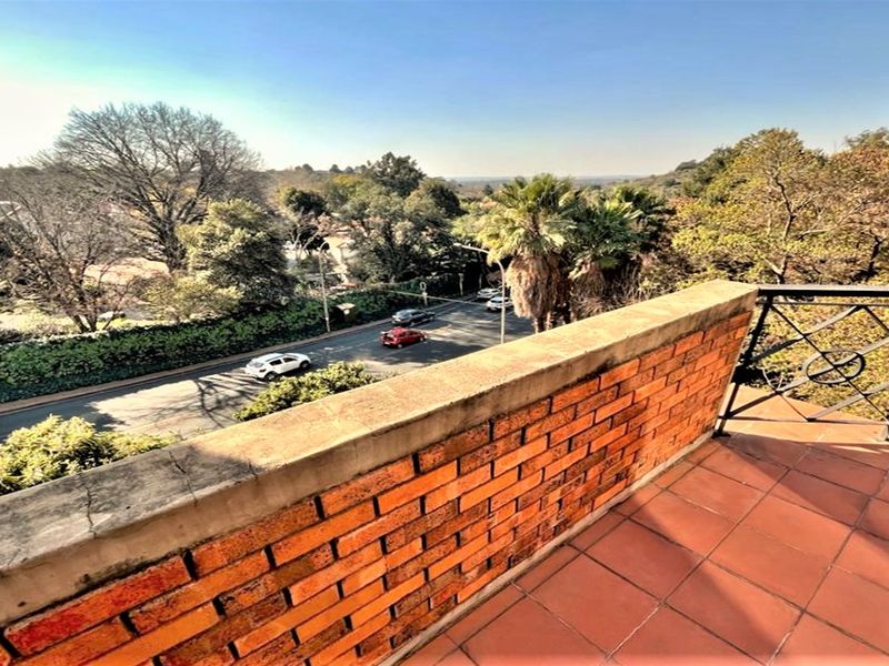 An elevated balcony featuring a brick parapet wall, terracotta tiling, and metal railings, offering an expansive view of the surrounding street and landscape.