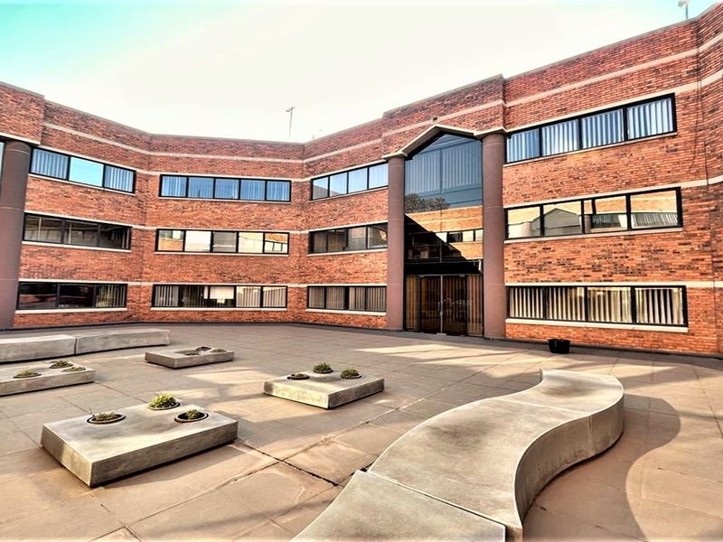 A well-maintained brick office building exterior featuring a paved courtyard with integrated concrete seating and large tinted windows.