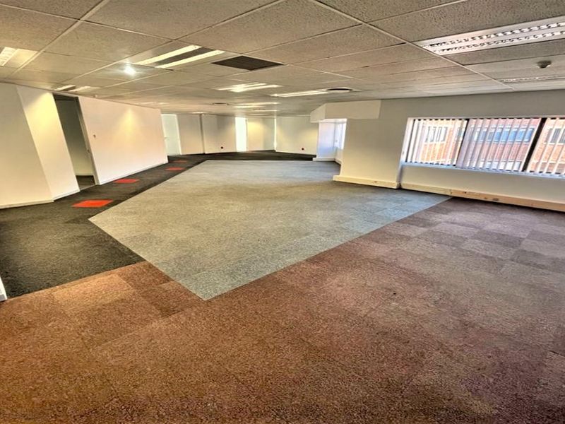 Spacious open-plan office area featuring suspended ceilings, recessed lighting, and multi-colored carpet tiles, offering a versatile workspace layout.